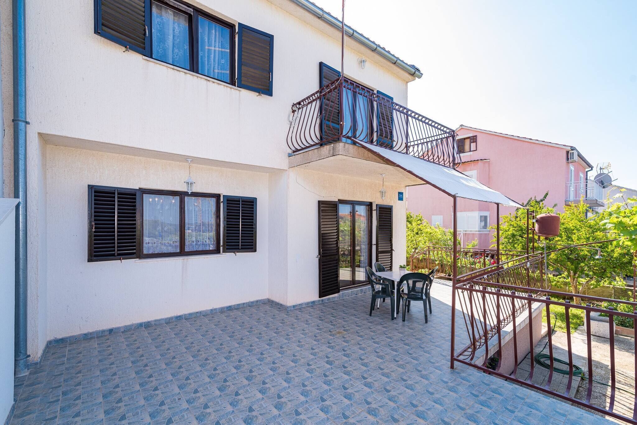 Edificio de dos pisos con patio empedrado, balcón con baranda de metal y una mesa con sillas.