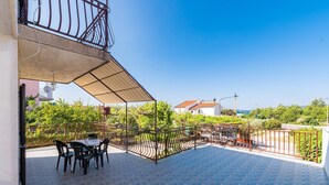 A covered outdoor patio with a table and chairs, surrounded by a metal fence and greenery.