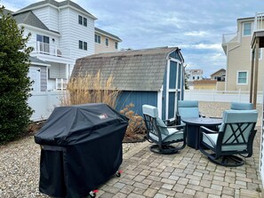 A patio area with a barbecue grill, outdoor seating, and a small shed. - Avalon 3BR Bayside Retreat: Sleeps 7, Large Porch, Outdoor Shower & Grill (Avalon)