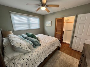 Quarto com cama, ventilador de teto, janela com persianas, porta e armário.