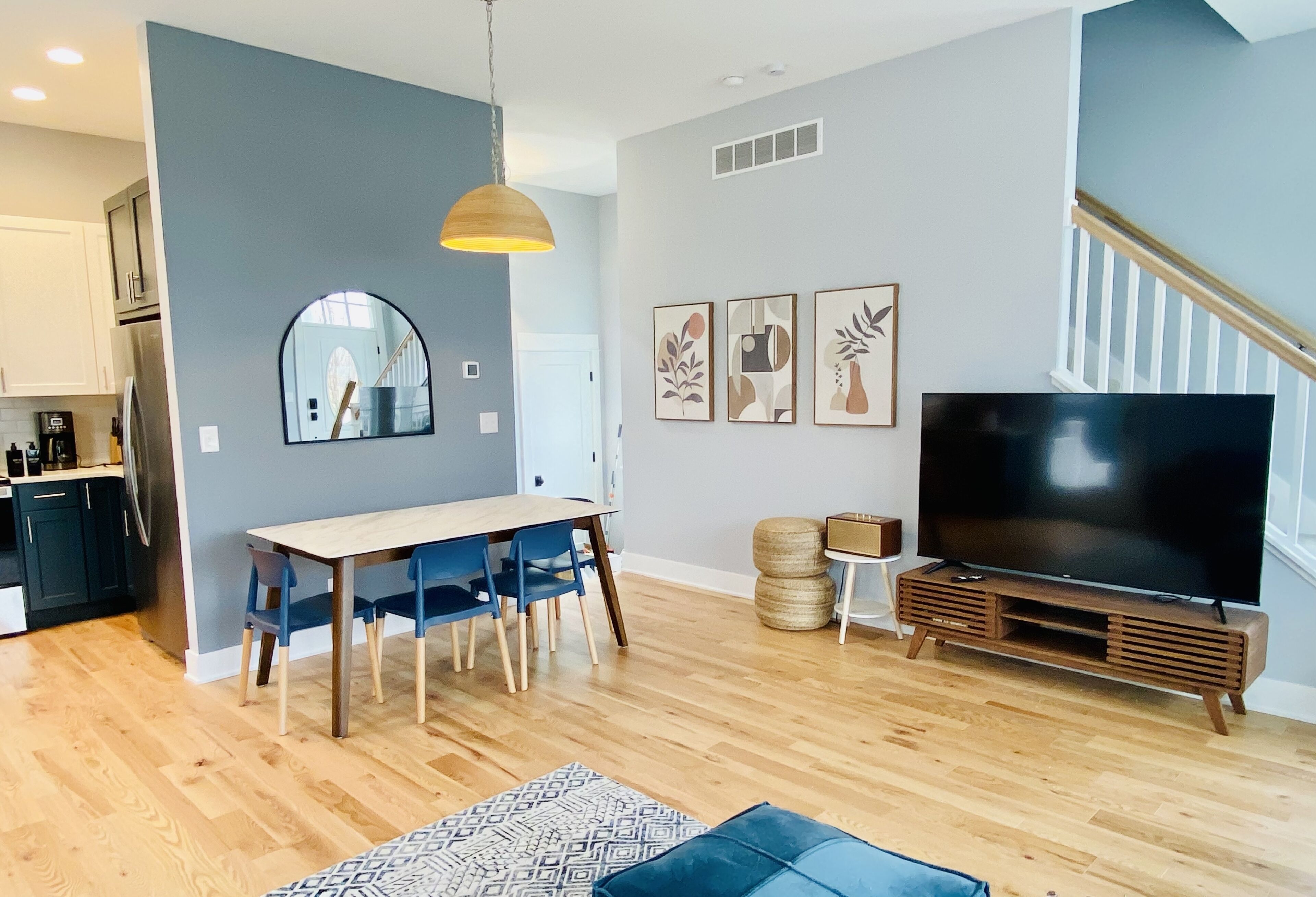 A modern living room with a dining area, a large flat-screen TV, and a staircase.