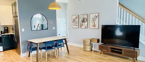 A modern living room with a dining area, a large flat-screen TV, and a staircase.