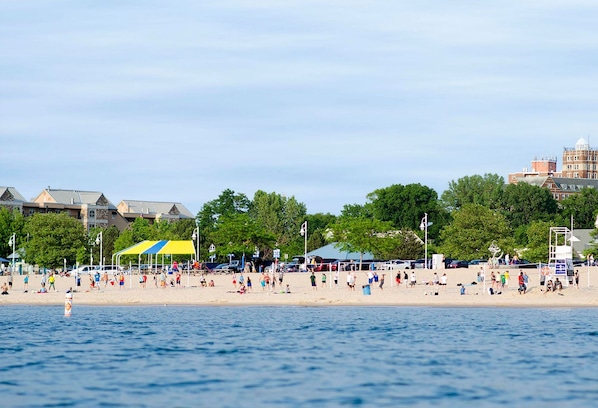 A beach with people, tents, and buildings in the background.