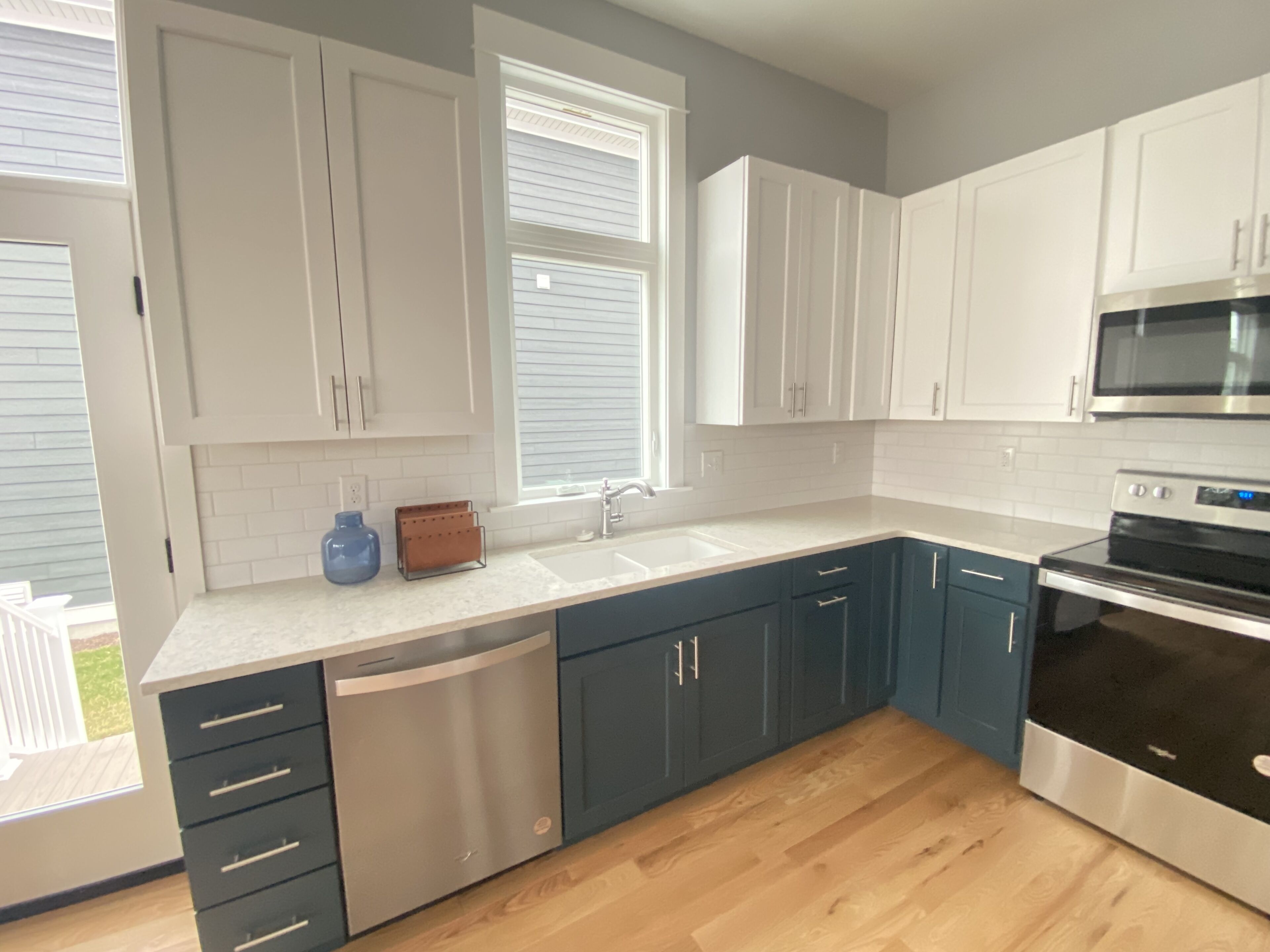 A modern kitchen with white and blue cabinets, a stainless steel dishwasher, and an oven.