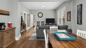 Een ruime woonkamer met een houten eettafel, grijze banken en een televisie.