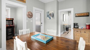 Een eetgedeelte met een houten tafel, witte stoelen, een spel, een koffieapparaat en een Mocha bord.