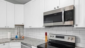 Een moderne keuken met witte kasten, een roestvrijstalen magnetron, een gasfornuis en een granieten aanrecht.