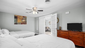 Ein Schlafzimmer mit zwei Betten, einem Deckenventilator, einem Fernseher und einer Holzkommode.