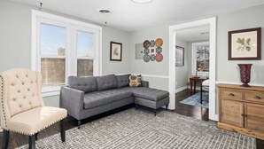 Ein Wohnzimmer mit einem Ecksofa, einem Samt-Sessel, einem gemusterten Teppich und einer Holzkabine.