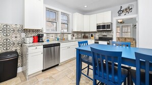 Una cocina moderna con armarios blancos, un lavavajillas de acero inoxidable y una mesa comedor azul con sillas a juego.