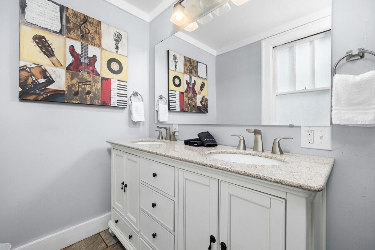 A bathroom with a double sink vanity, white cabinets, and a large mirror. There are towels hanging on the wall and a painting above the mirror.