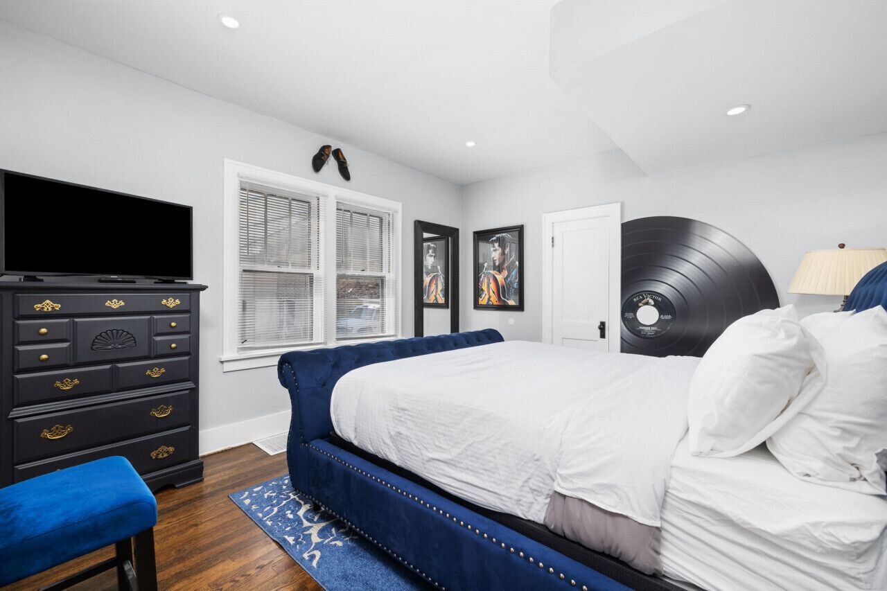 Un dormitorio con cama, cómoda, televisor y obras de arte.