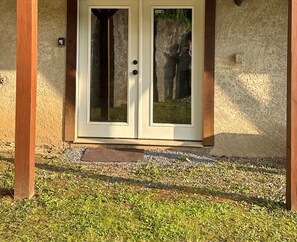 Puerta doble con panel de vidrio, ubicada en una pared texturizada, que da a un área de grava y césped.