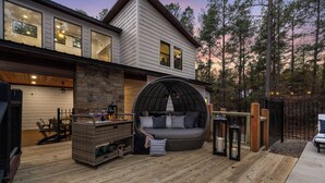 A cozy outdoor seating area with a wicker sofa and a stone fireplace, surrounded by a wooden deck and a stone wall.