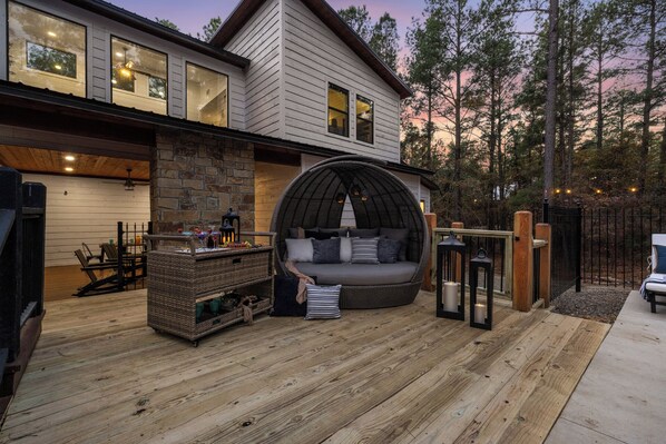 Un espace extérieur accueillant, avec un canapé en osier et une cheminée en pierre, entouré d’une terrasse en bois et d’un mur de pierre.