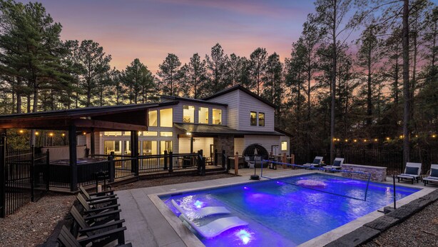 A two-story house with a swimming pool, deck chairs, and a covered patio area.