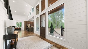 A spacious interior with a wooden floor, a dining area with a table and chairs, a kitchen with wooden cabinets, and large windows offering a view of the outdoors.