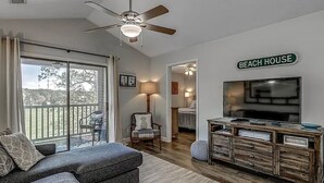 A living room with a sofa, a TV, a ceiling fan, and a sign that reads "Beach House".