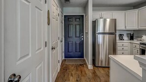 A narrow hallway with white doors, a blue door, and a stainless steel refrigerator.