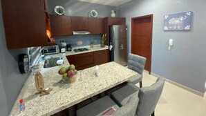 Una cocina moderna con encimeras de granito, electrodomésticos de acero inoxidable y una zona de comedor con mesa de mármol y sillas tapizadas en gris.