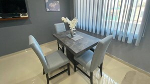 Un comedor con una mesa, sillas, un jarrón con flores, un televisor de pantalla plana y una ventana con persianas.