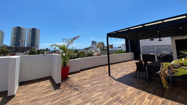 Una terraza en la azotea con suelo de madera, un área de estar cubierta y vistas de edificios de la ciudad.