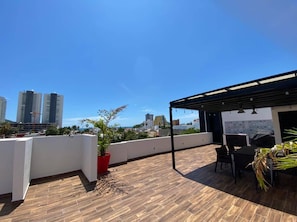 A rooftop terrace with a wooden floor, a covered seating area, and a view of city buildings. - Islas G203 ByTrvl2hm & Mazatlan Regency (Mazatlán)