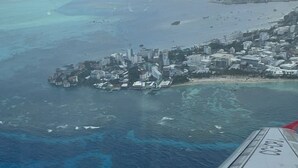 Une vue aérienne d’une ville côtière, avec des bâtiments situés près du rivage, une mer bleue et limpide et un ciel nuageux.
