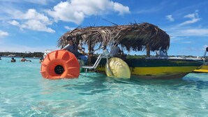 Un bateau doté d’un toit de chaume et de flotteurs gonflables, naviguant dans une eau turquoise et cristalline.