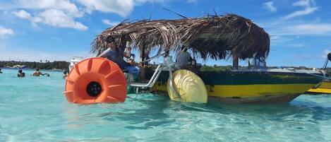 A boat with a thatched roof and inflatable floats in clear turquoise water.