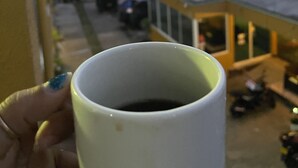 Une main tenant une tasse, avec en arrière-plan un coucher de soleil et des palmiers.