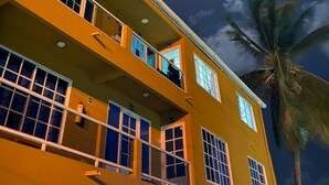 Un immeuble à plusieurs étages, doté de balcons et de grandes fenêtres, se dressant sous un ciel nocturne où l’on peut apercevoir la lune.