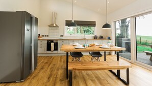 Une cuisine moderne avec un réfrigérateur en acier inoxydable, une table à manger en bois, des chaises noires et des luminaires suspendus.