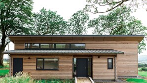 Une maison moderne à deux étages, dotée d’un toit plat, de grandes fenêtres et d’une façade en bois.