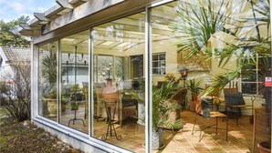 Ein Wintergarten mit Glaswänden, Korbmöbeln und Topfpflanzen.