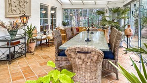 Ein Wintergarten mit einem großen Tisch, Korbstühlen und Kübelpflanzen.