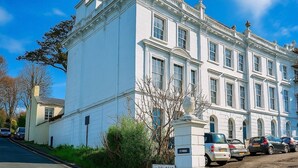 A large white building with multiple windows and a statue on the corner. - Stunning Top Floor Flat | Pet Friendly | Sea Views (Torquay)