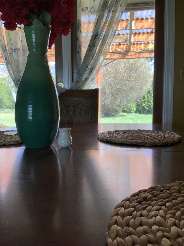 A teal vase with red flowers on a wooden table, a white pitcher, and a woven placemat. - Cozy cabin style home in a quiet neighborhood in terrace hgts. (Yakima)