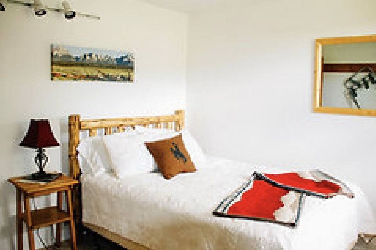 Ein Schlafzimmer mit einem hölzernen Bett, weißer Bettwäsche, einer roten Decke, einer Lampe und einem Bild an der Wand.