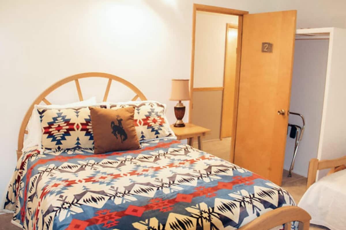 Ein Schlafzimmer mit einem Bett, einem Nachttisch, einer Lampe, einer Tür und einem Stuhl.