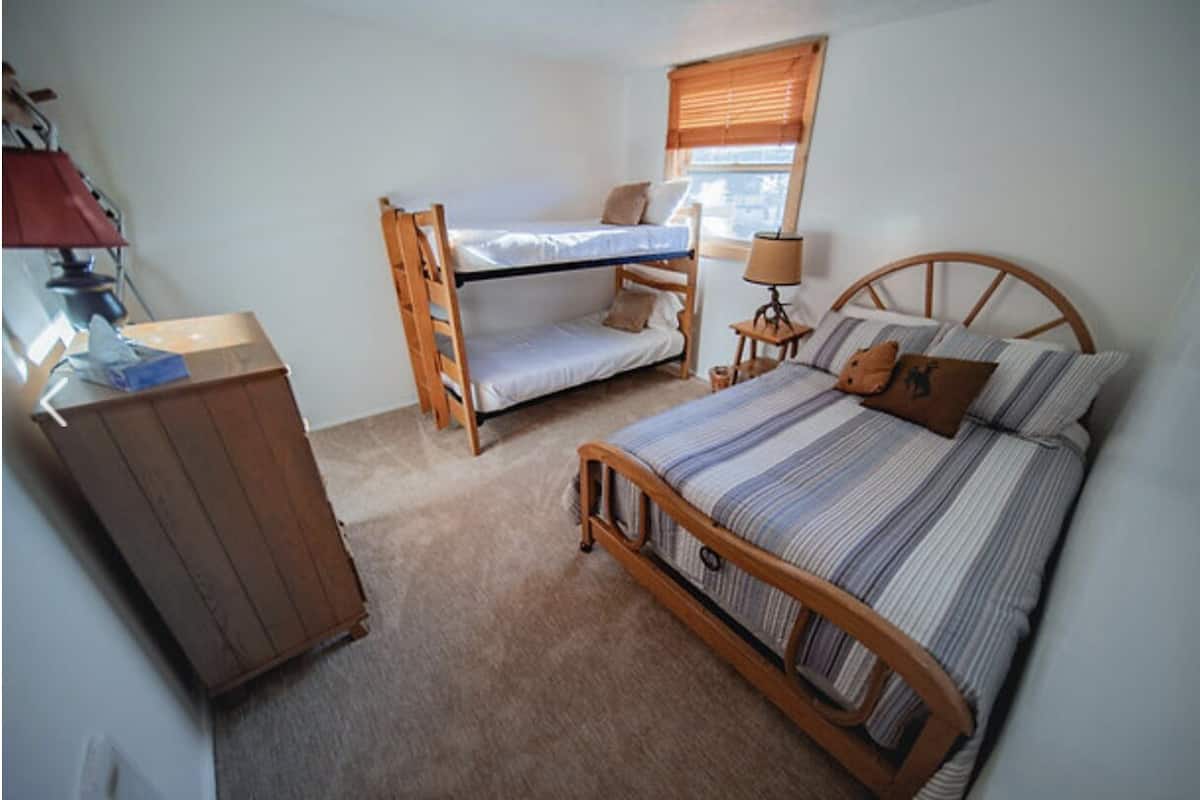 Ein Schlafzimmer mit einem Etagenbett, einem Einzelbett, einem Holzschrank und einem Fenster mit Jalousien.