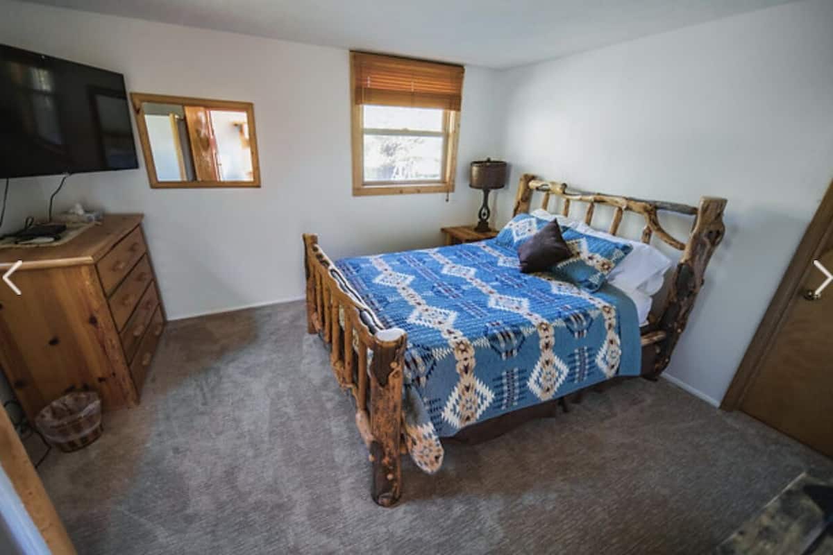 Ein Schlafzimmer mit einem Holzbett, einem Schminktisch, einem Fernseher, einem Fenster mit Jalousien und einer Lampe.