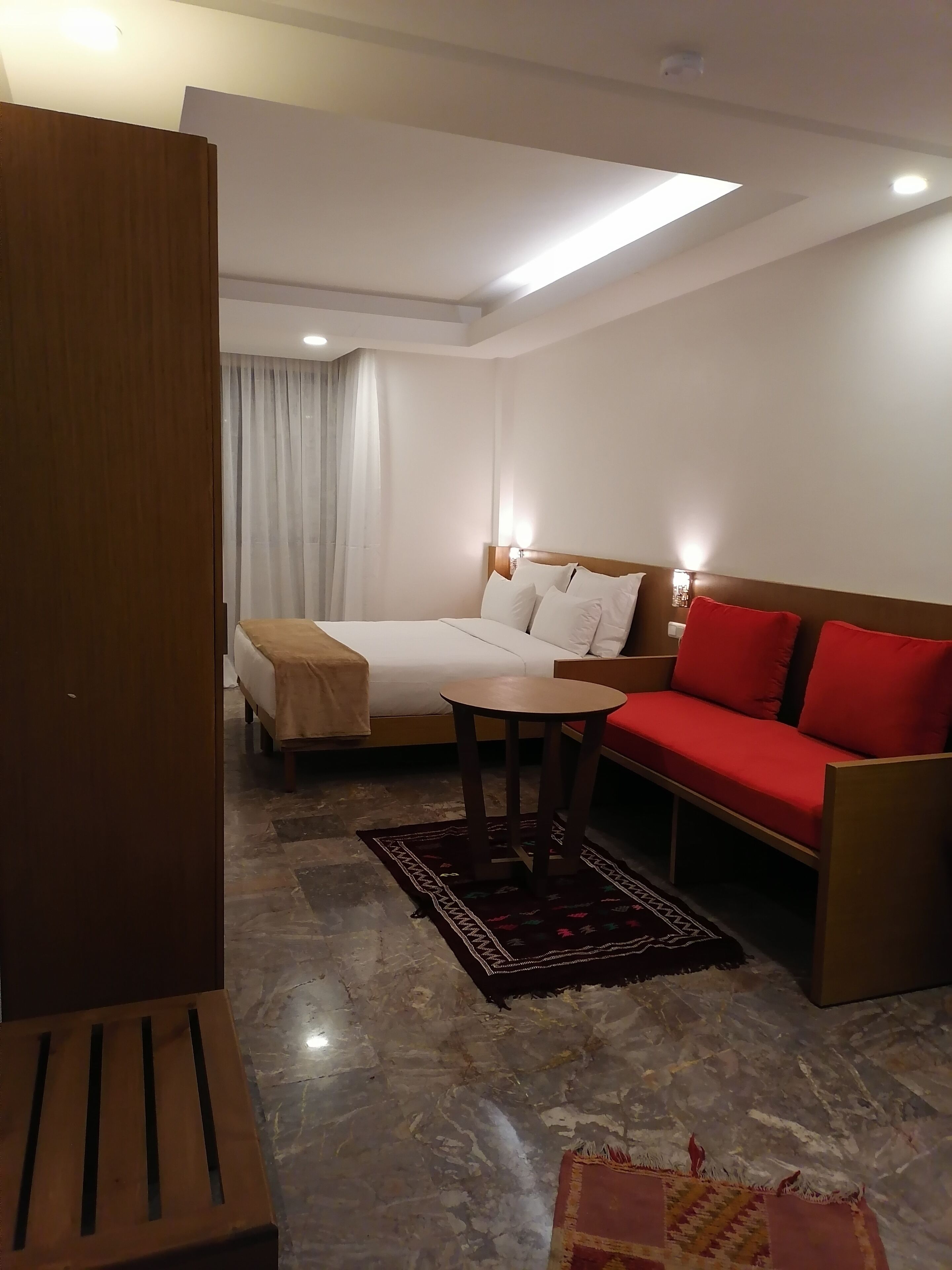 A hotel room with a bed, a sofa, a small table, and a wooden bench.