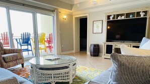 A living room with a glass-top coffee table, a sofa, colorful chairs, and a flat-screen TV. -   GULF FRONT 2 bed 2 bath 1700 sq ft with amazing amenities! 2 master king suite (Orange Beach)