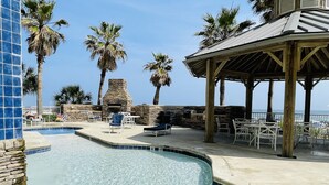A pool area with lounge chairs and a stone fireplace. -   GULF FRONT 2 bed 2 bath 1700 sq ft with amazing amenities! 2 master king suite (Orange Beach)