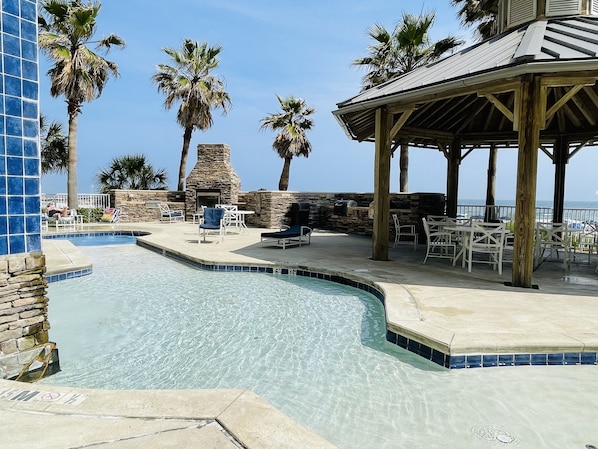 A pool area with lounge chairs and a stone fireplace.