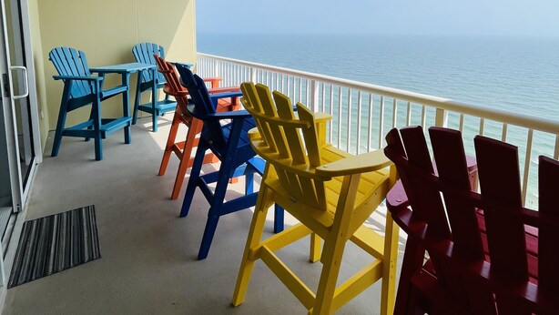 A balcony with colorful Adirondack chairs facing a view of the ocean. -   GULF FRONT 2 bed 2 bath 1700 sq ft with amazing amenities! 2 master king suite (Orange Beach)