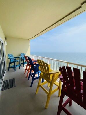 A balcony with colorful Adirondack chairs facing a view of the ocean.