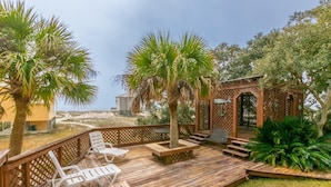 Une terrasse en bois avec des chaises longues, une pergola en bois et une vue sur la plage et l’océan.