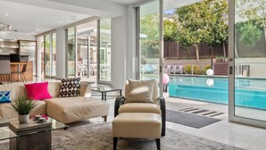 Ein modernes Wohnzimmer mit Sofa, Sessel und Couchtisch. Ein großes Glasfenster führt zu einem Poolbereich.